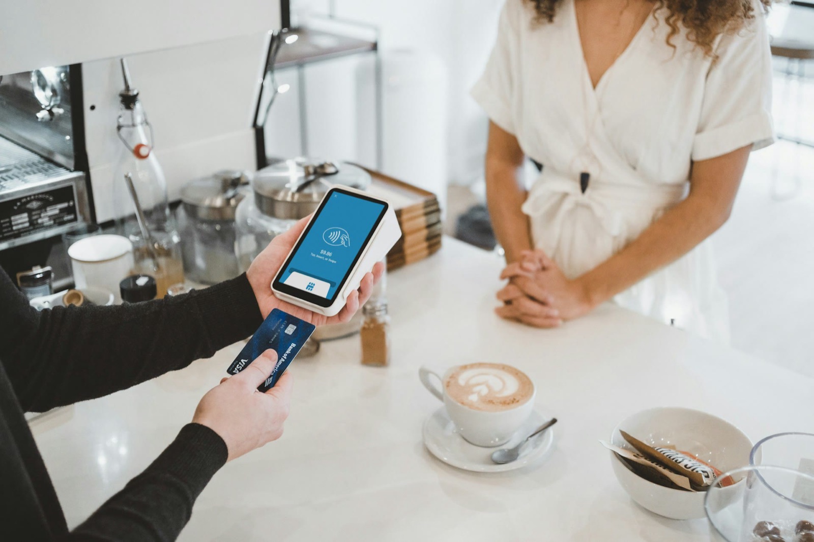 A barista hands a card reader across the counter of a coffee shop